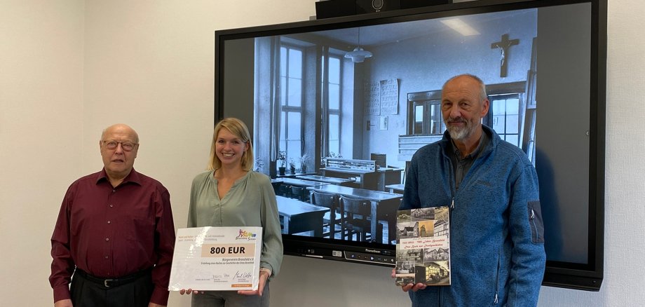 Martina Wassong, 1. Vorsitzende des Bürgervereins Bronsfeld (m.) nahm gemeinsam mit Artur Stoff (l.), der die Chronik mit Frajp Erben-Floeth (r.) gestaltete, den Förderscheck der Bürgerstiftung im Schleidener Rathaus entgegen.