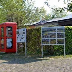 Der Harperscheider Dorfplatz mit Bücherselbstausleihe in einer ausrangierten Telefonzelle und Luftbildern bzw. Routenkarte des zwölf Kilometer langen Flurschilderwanderweges rund ums Doppeldorf. 