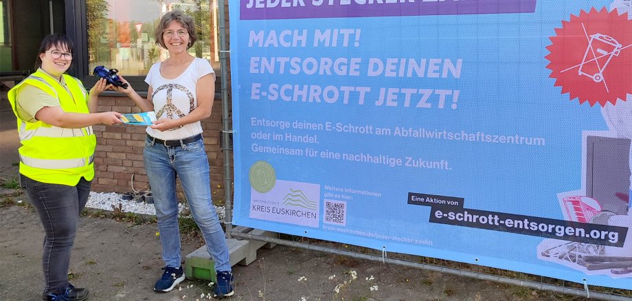 Für mitgebrachten Elektroschrott, wie dem kaputten Föhn, bekommt Frau Ude von AWZ-Mitarbeiterin eine Samentüte mit Bienen- und Schmetterlingsfreundlichem Saatgut geschenkt (links: Brigitte Ohlerth; rechts: Ruth Claudia Ude).