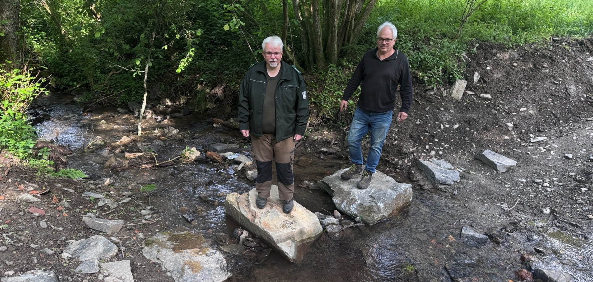 Markus Vollmer vom Bundesforstbetrieb Rhein-Weser (links) und Eckhard Jäck, Leiter der Holzbauwerkstatt der Nationalparkverwaltung (rechts) testen die neuen, naturbelassenen Trittsteine im erfolgreich renaturierten Bachbett des Sauerbachs. Markus Vollmer vom Bundesforstbetrieb Rhein-Weser (links) und Eckhard Jäck, Leiter der Holzbauwerkstatt der Nationalparkverwaltung (rechts) testen die neuen, naturbelassenen Trittsteine im erfolgreich renaturierten Bachbett des Sauerbachs.