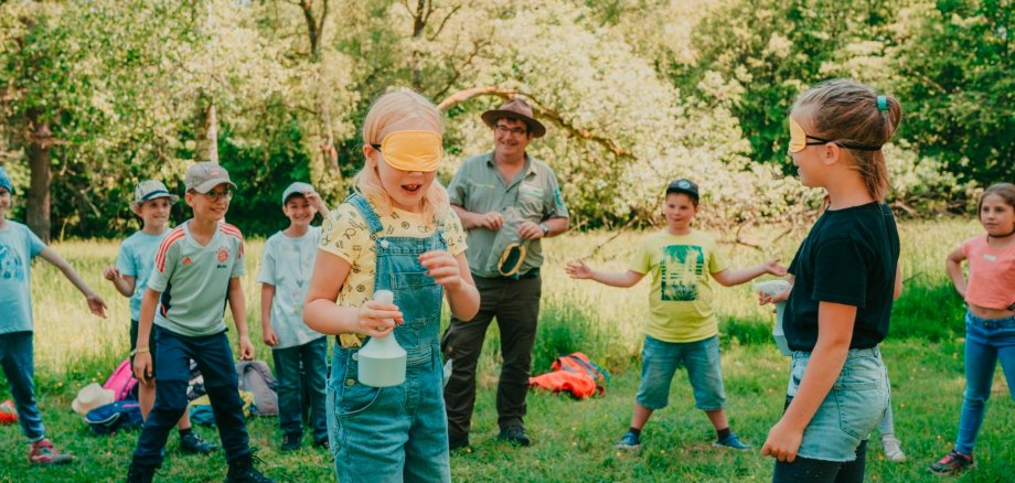 Mit den Sinnen einer Fledermaus auf Insektenjagd. Beim Fledermausspiel versuchen Kinder mit verbundenen Augen auf feinste Hörzeichen in ihrer Umgebung zu achten, um sich kein Nachtfalter – hier die umstehenden Kinder, - entgehen zu lassen.