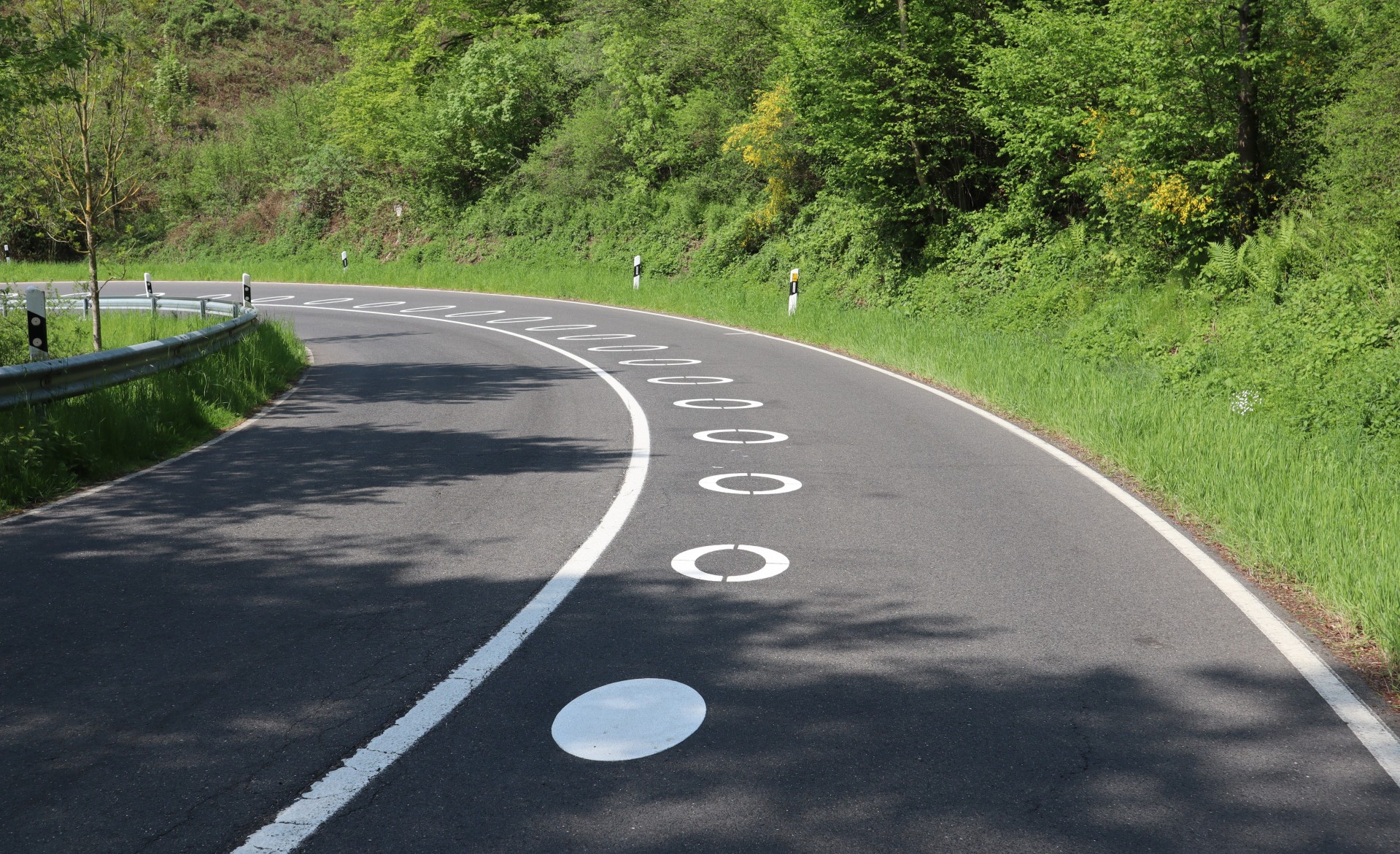 Die weißen Kreise zeigen eine sichere Fahrlinie an. Wer sich daran hält, kommt nicht in den Gegenverkehr und hält genügend Abstand zu entgegenkommenden Fahrzeugen. Das Foto stammt vom Pilotprojekt 2023 an der Panoramastraße im Kreis Düren. Auf der L234 bei Bad Münstereifel sollen die Kreise Ende Mai / Anfang Juni aufgebracht werden.