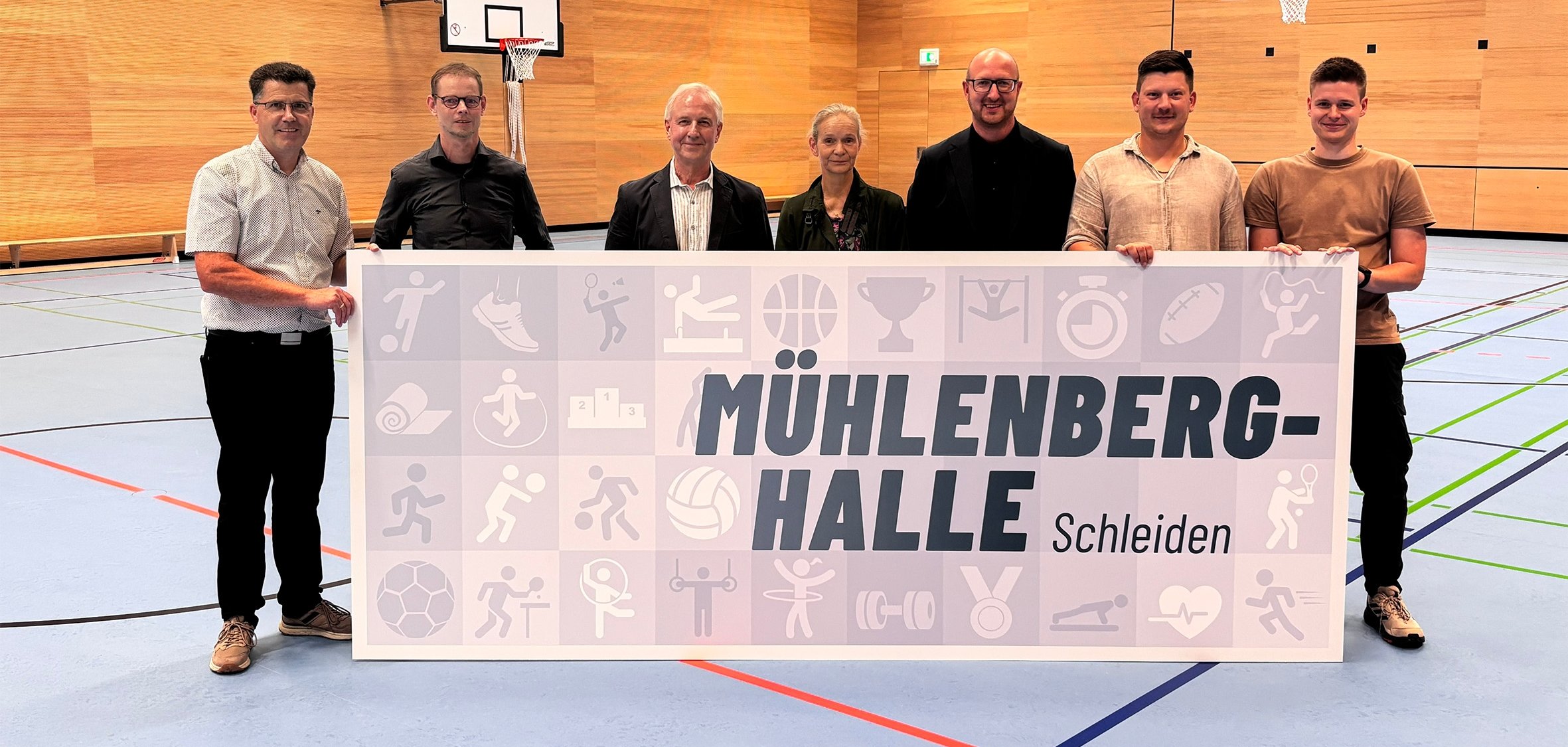 23/2026 - Bild 01: Mit der Enthüllung des neuen Schildes wurde die Mühlenberghalle im Rahmen der Eröffnung offiziell benannt. v.l.: Armin Fischbach (Fachbereichsleiter Hochbau), Marcus Bierschenk (Büro abph Heimbach), Wolfgang Schmitz (Schulleiter der Astrid-Lindgren-Schule), Lene Drude (Lehrerin der Grundschule Schleiden), Bürgermeister Ingo Pfennings, Felix Stoff (Stadt Schleiden, Hochbau) und Sven Löhr (Lehrkraft der Grundschule Schleiden). (© Anja Breuer / GfW Schleiden)
