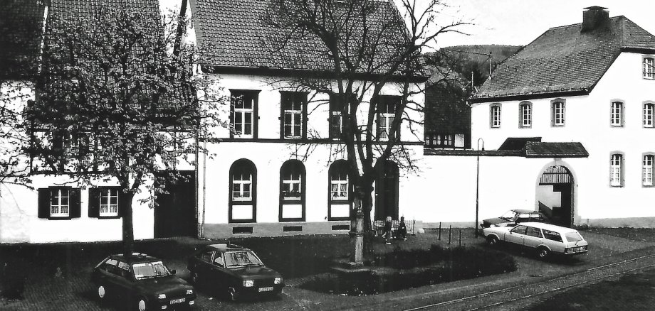 Das mittlere Gebäude, unmittelbar am Dorfplatz gelegen, wurde in den Jahren 1834/35 als erste Olefer Dorfschule errichtet und als solche bis 1926 genutzt. Nach einer grundlegenden Sanierung in den 1980er Jahren erstrahlt das heutige Wohnhaus in neuem Glanz.