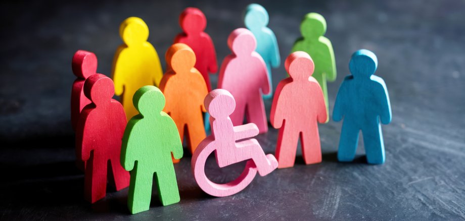 Bunte Gruppe von hölzernen Menschenfiguren unterschiedlicher Farbe, darunter Rollstuhlfahrer.