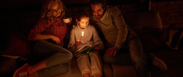 Familie sitzt auf dem Sofa ohne Strom mit Kerzen und lesen ein Buch.